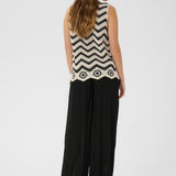 Woman wearing a sleeveless black and white patterned top with wide-leg pants on a white background