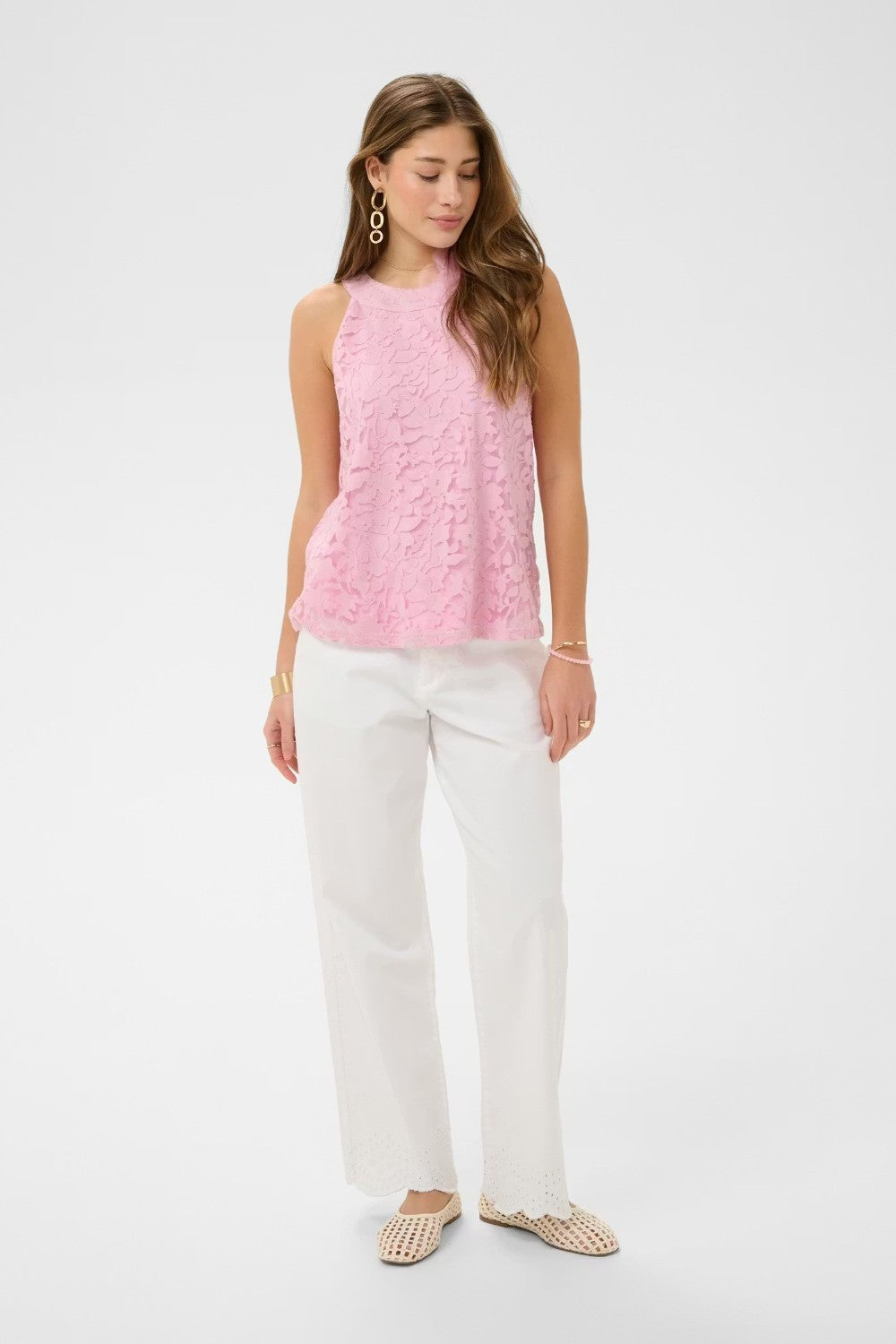 Woman wearing a pink sleeveless top and white pants on a white background