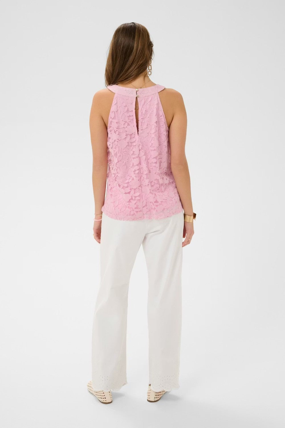 Woman wearing a pink sleeveless top and white pants on a white background