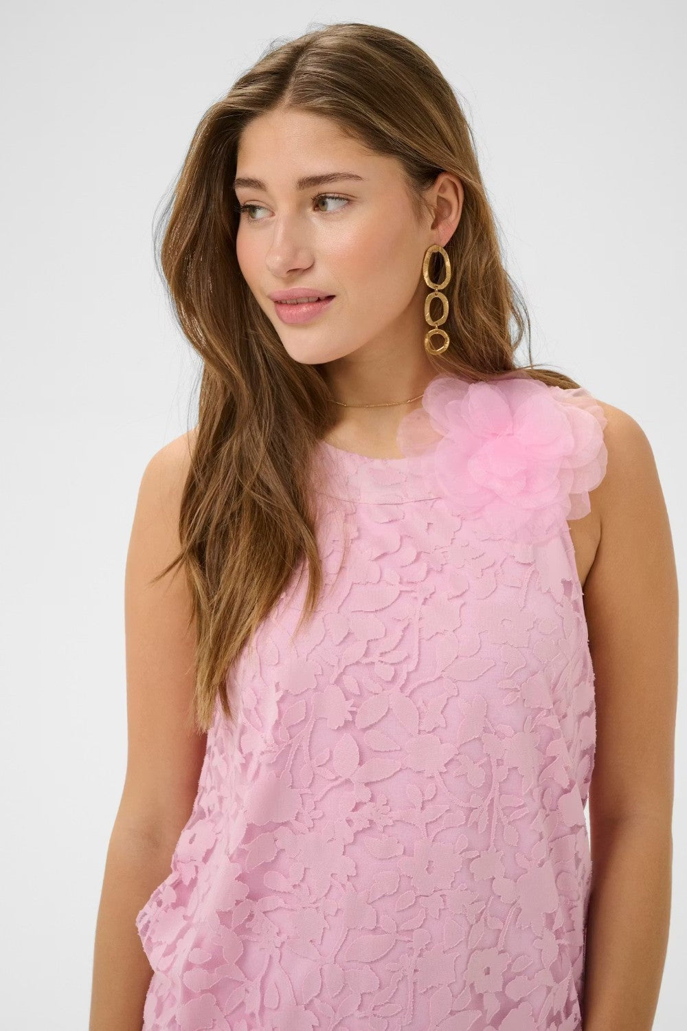 Woman wearing a pink lace dress with floral details on a white background