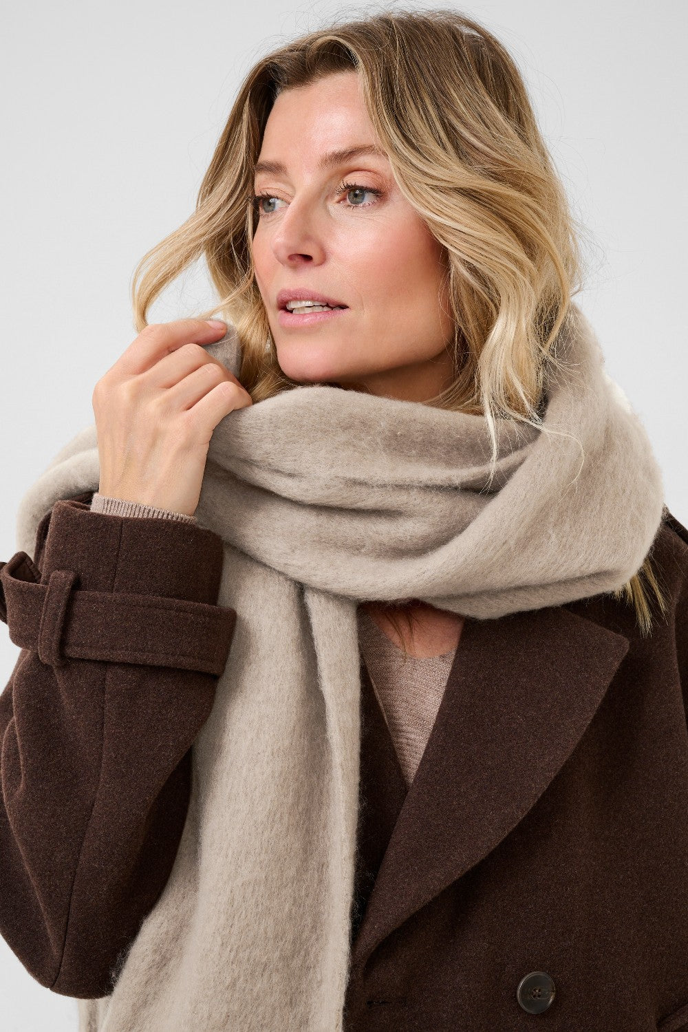 Woman wearing a beige scarf and brown coat against a white background