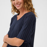 Woman wearing a navy pleated top against a white background