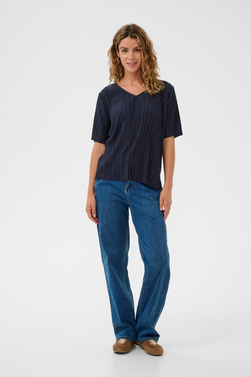 Woman wearing a navy blue top and blue jeans on a white background