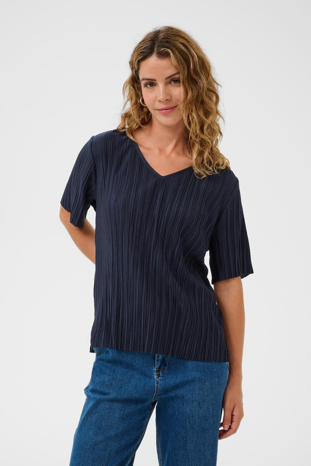 Woman wearing a navy pleated top and blue jeans on a white background