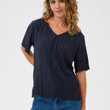 Woman wearing a navy pleated top and blue jeans on a white background