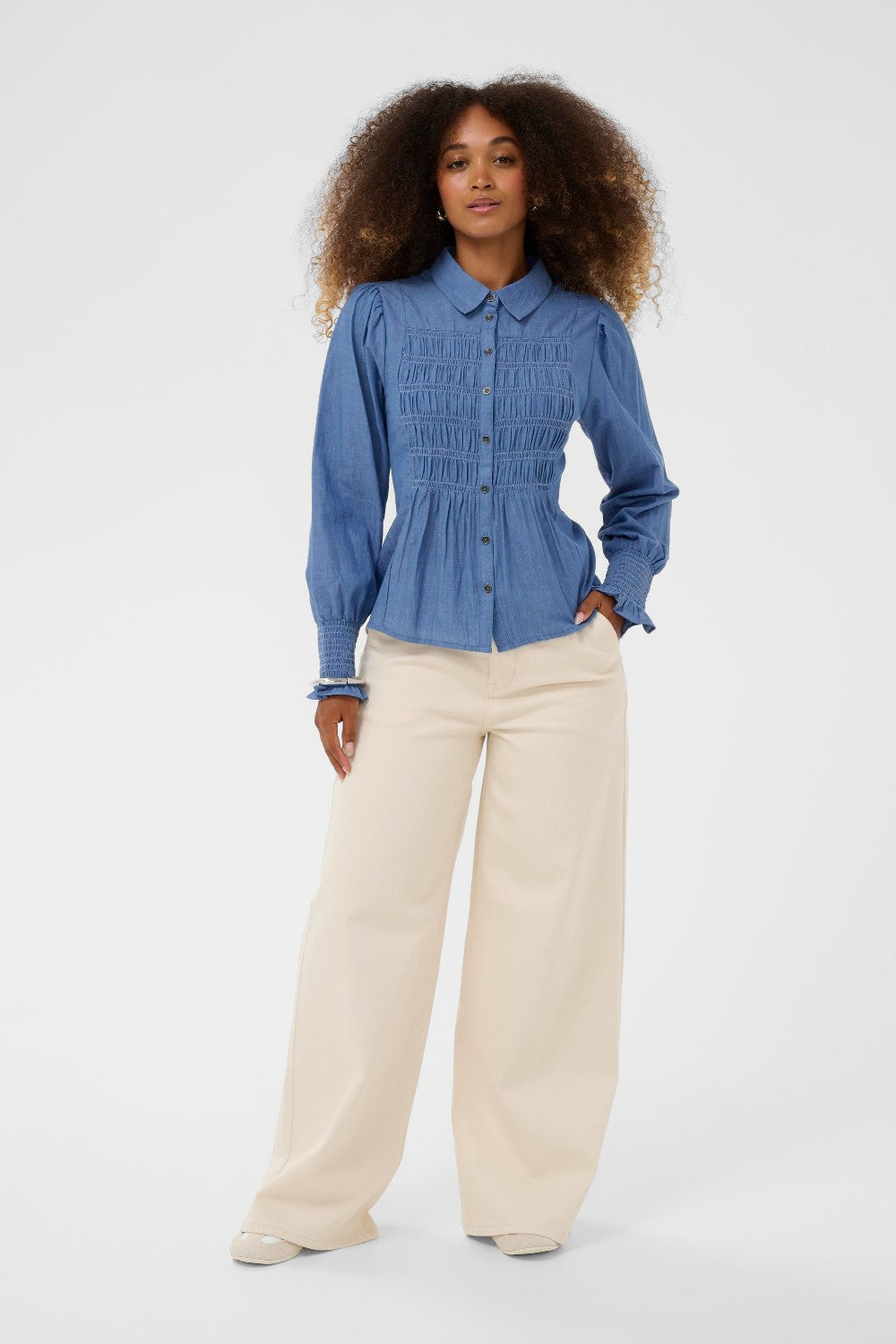 Woman wearing a blue shirt and beige pants on a white background