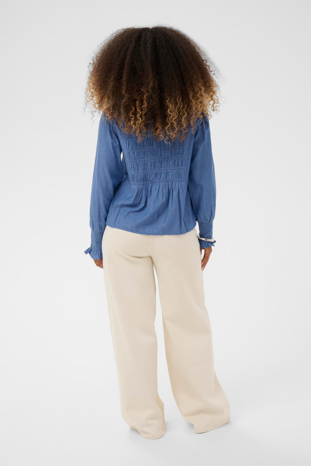 Person wearing a blue blouse and beige pants on a white background