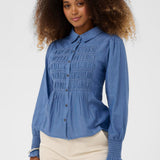 Woman wearing a blue blouse with smocked details on a white background