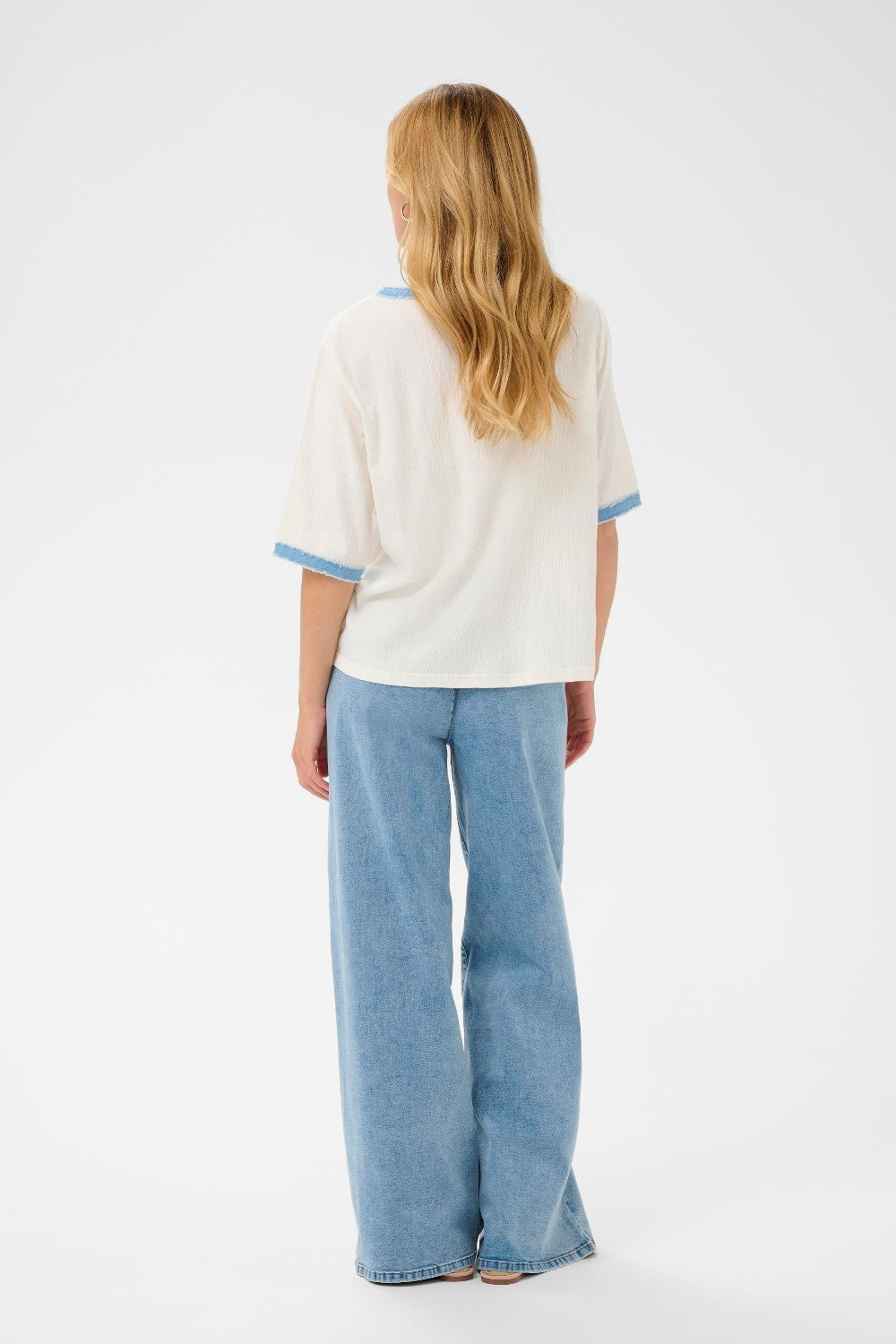 Person wearing a white top with blue trim and blue jeans on a white background
