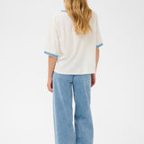 Person wearing a white top with blue trim and blue jeans on a white background