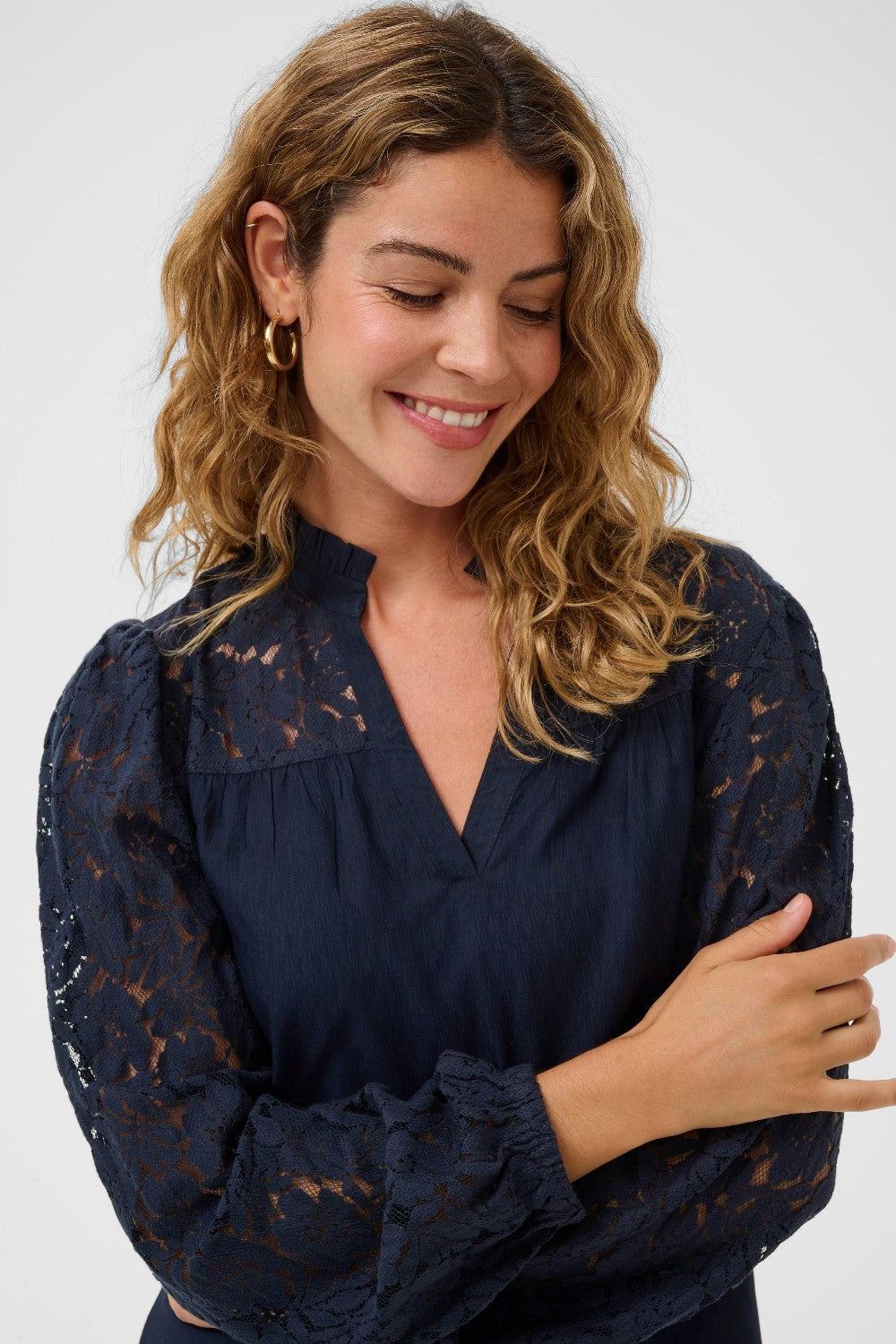 Woman wearing navy blouse with lace detail on shoulder and sleeve on white background