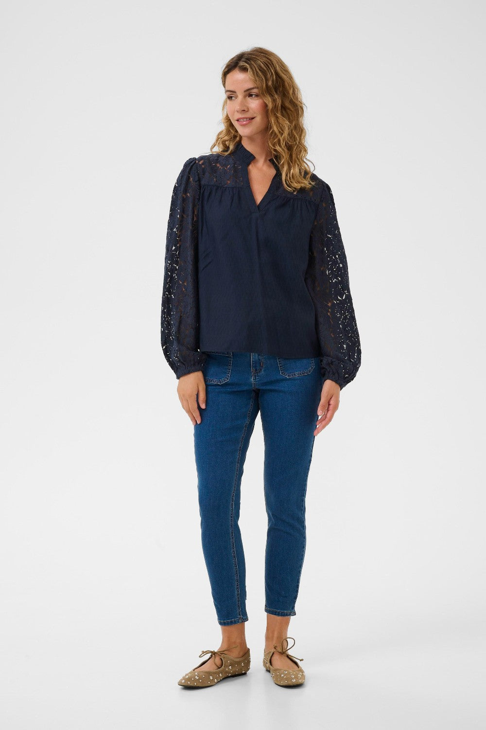 Woman wearing a dark blue blouse with lace sleeves and blue jeans on a white background