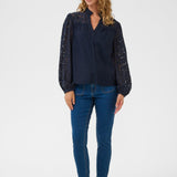 Woman wearing a dark blue blouse with lace sleeves and blue jeans on a white background