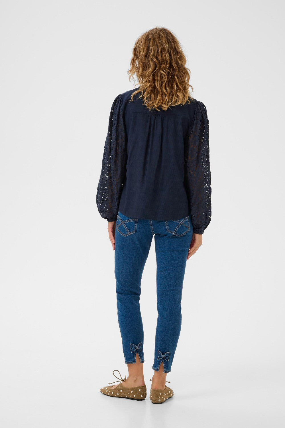 Person wearing a navy blouse with lace sleeves and blue jeans on a white background