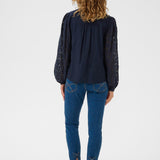 Person wearing a navy blouse with lace sleeves and blue jeans on a white background