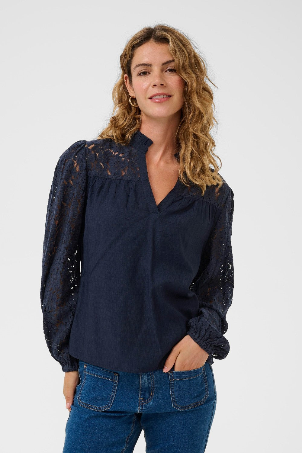 Woman wearing a navy blouse with lace details and blue jeans on a white background