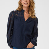 Woman wearing a navy blouse with lace details and blue jeans on a white background