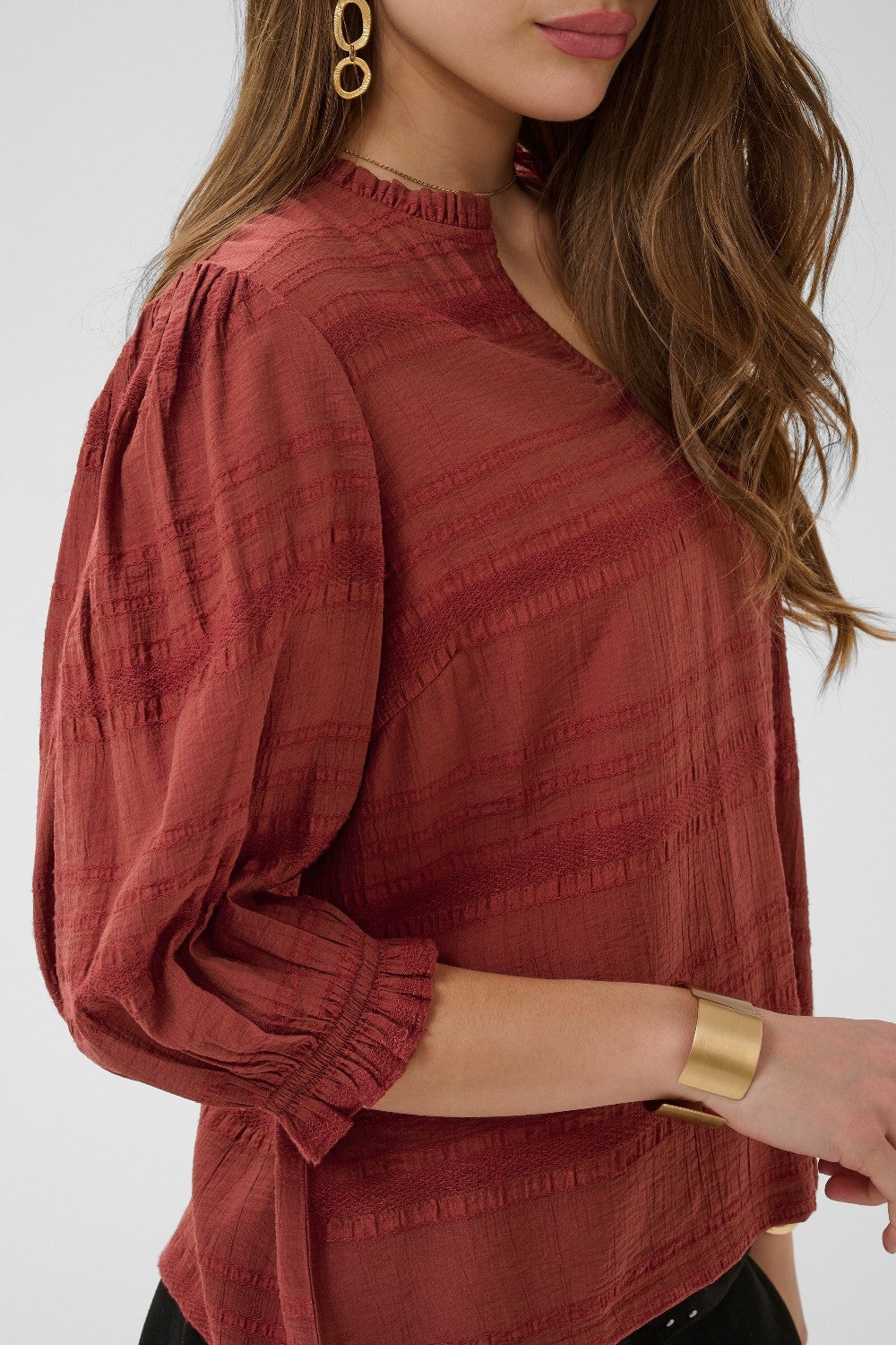 Woman wearing a red textured blouse with long sleeves against a white background