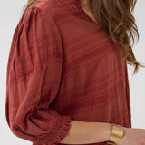 Woman wearing a red textured blouse with long sleeves against a white background