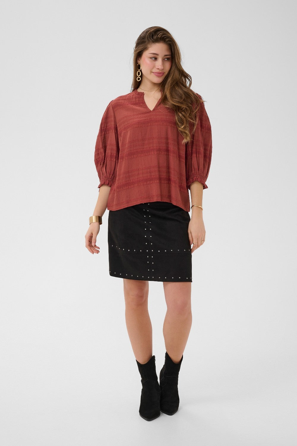 Woman wearing a rust-colored top and black skirt with studs on a white background