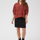 Woman wearing a rust-colored top and black skirt with studs on a white background