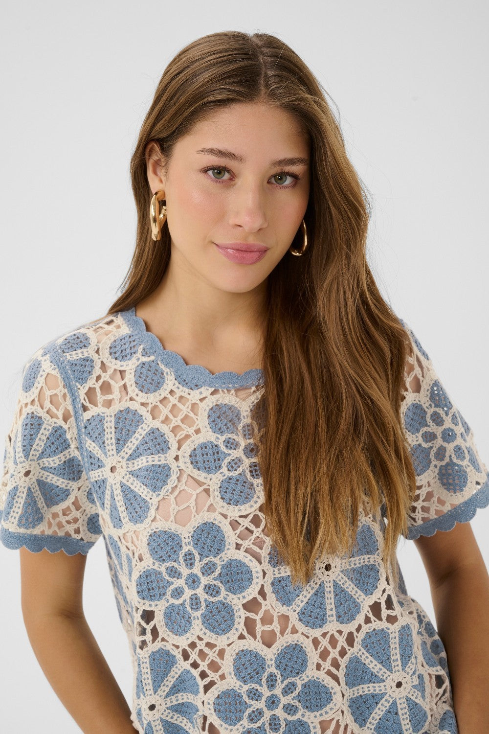 Woman wearing a blue and white floral crochet top against a plain background