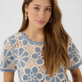 Woman wearing a blue and white floral crochet top against a plain background