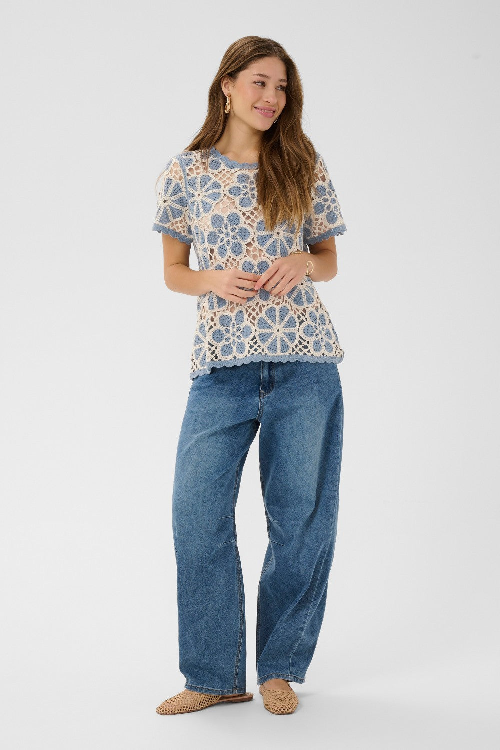 Woman wearing a patterned top and blue jeans on a white background