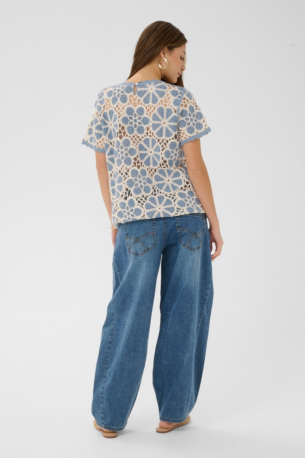 Woman wearing a patterned top and blue jeans on a white background