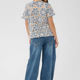 Woman wearing a patterned top and blue jeans on a white background