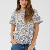 Woman wearing a floral lace top with blue and beige pattern on a white background
