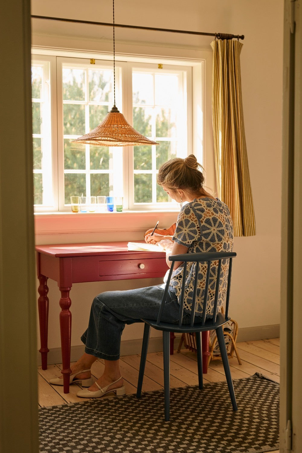 Person sitting at a desk by a window, writing in a notebook.