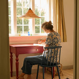 Person sitting at a desk by a window, writing in a notebook.