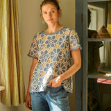 Woman wearing a floral crochet top and jeans standing in a room with a cabinet and curtains.