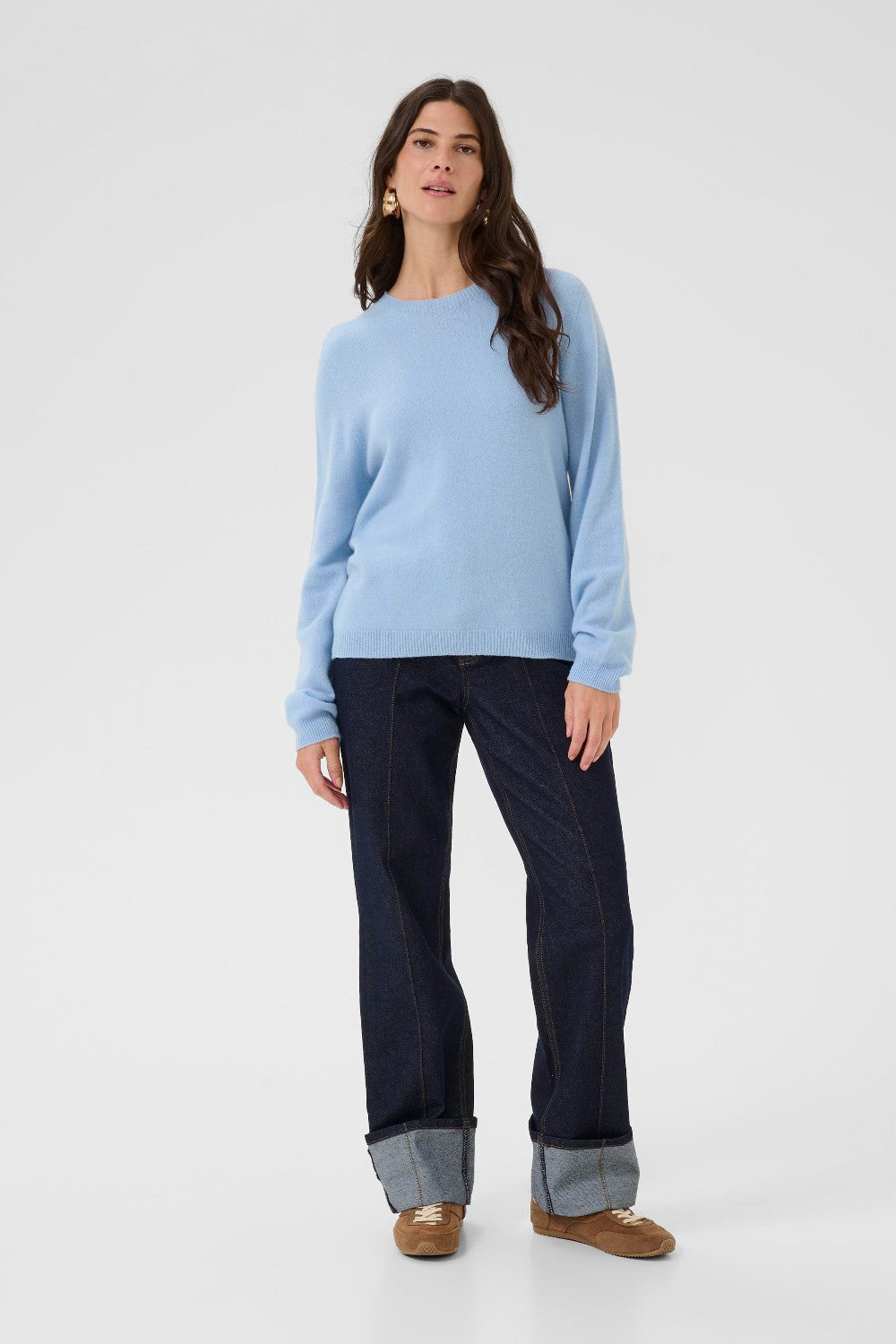 Woman wearing a light blue sweater and dark jeans on a white background
