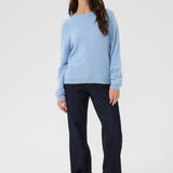 Woman wearing a light blue sweater and dark jeans on a white background