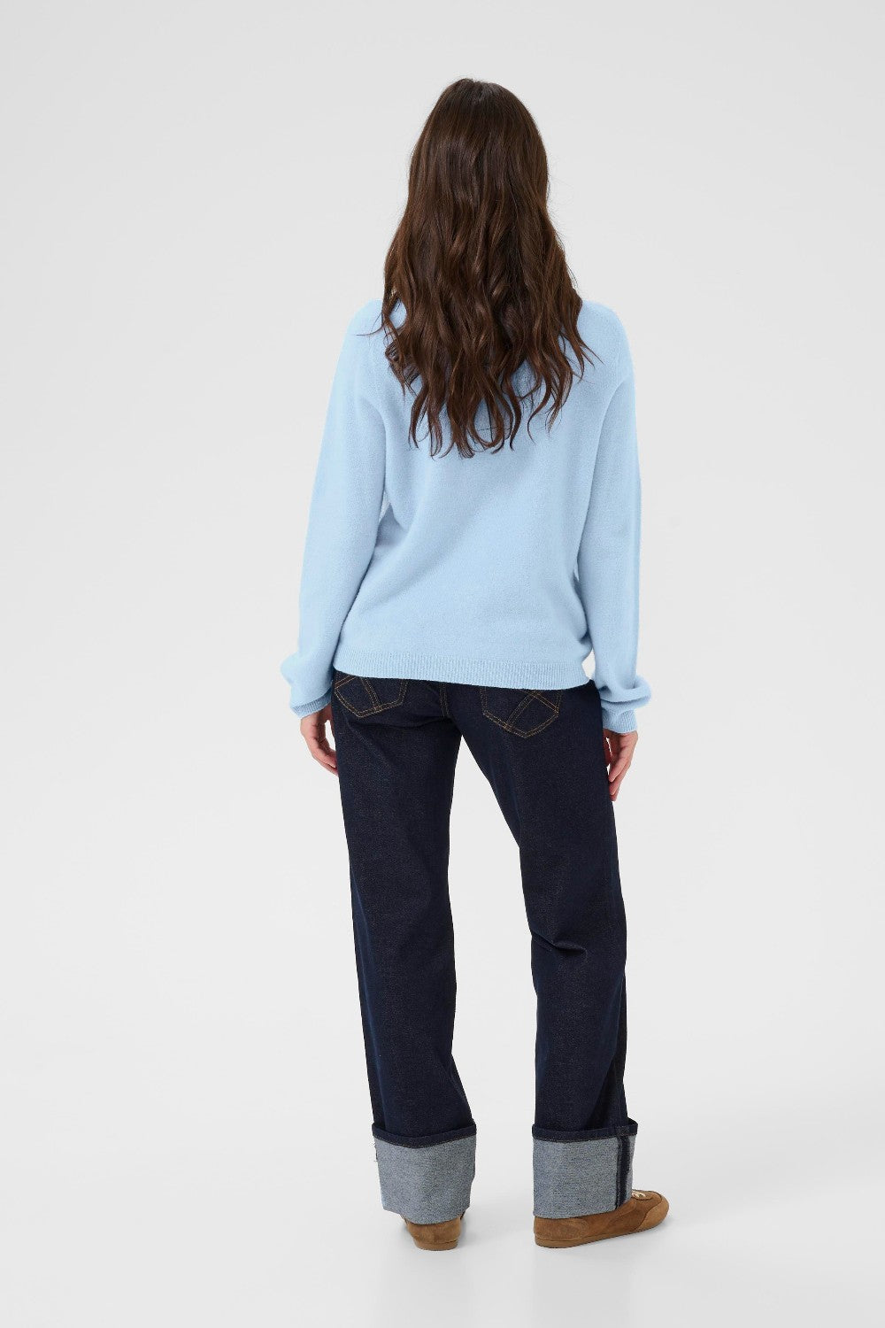 Person wearing a light blue sweater and dark pants on a white background