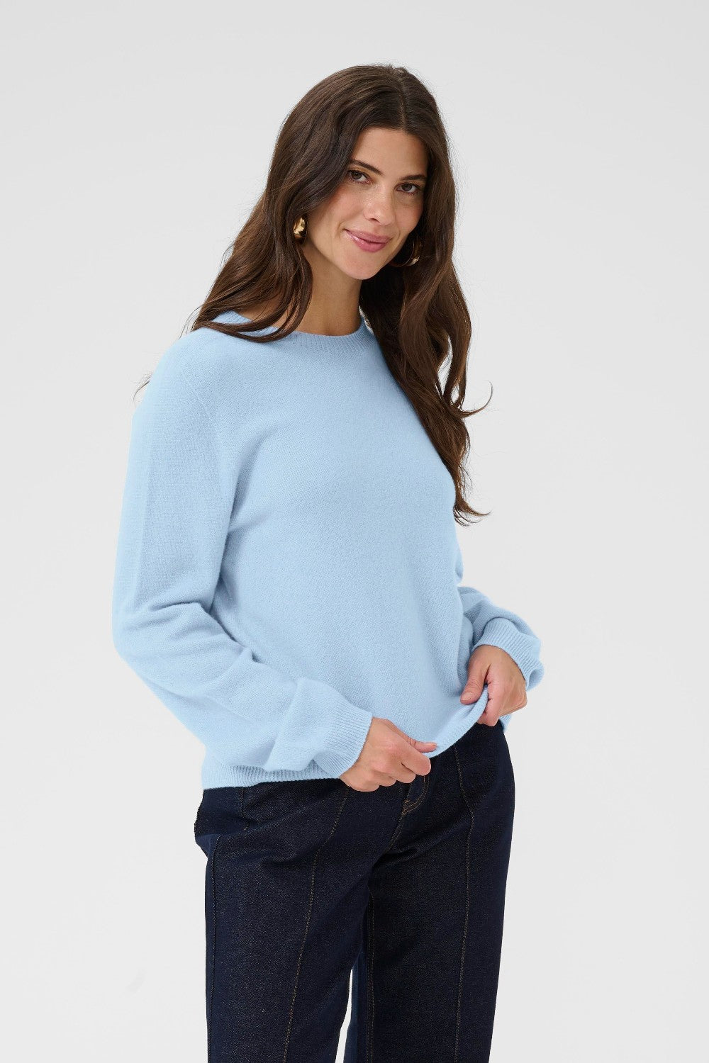 Woman wearing a light blue sweater and dark pants on a plain background