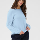 Woman wearing a light blue sweater and dark pants on a plain background
