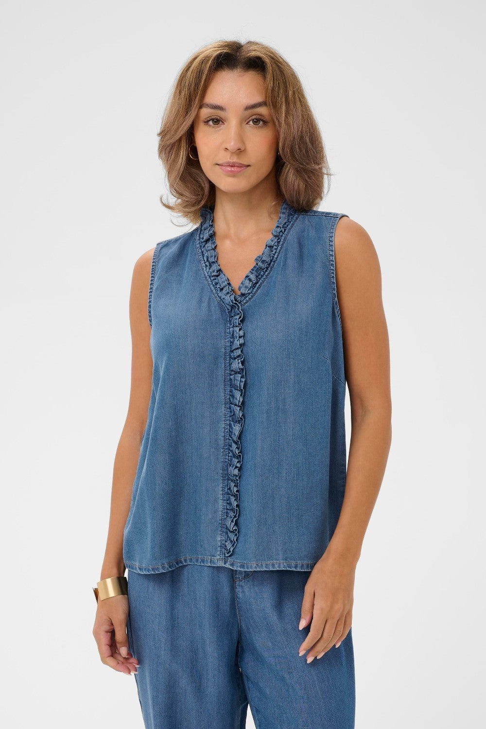 Woman wearing a sleeveless denim top and pants on a white background