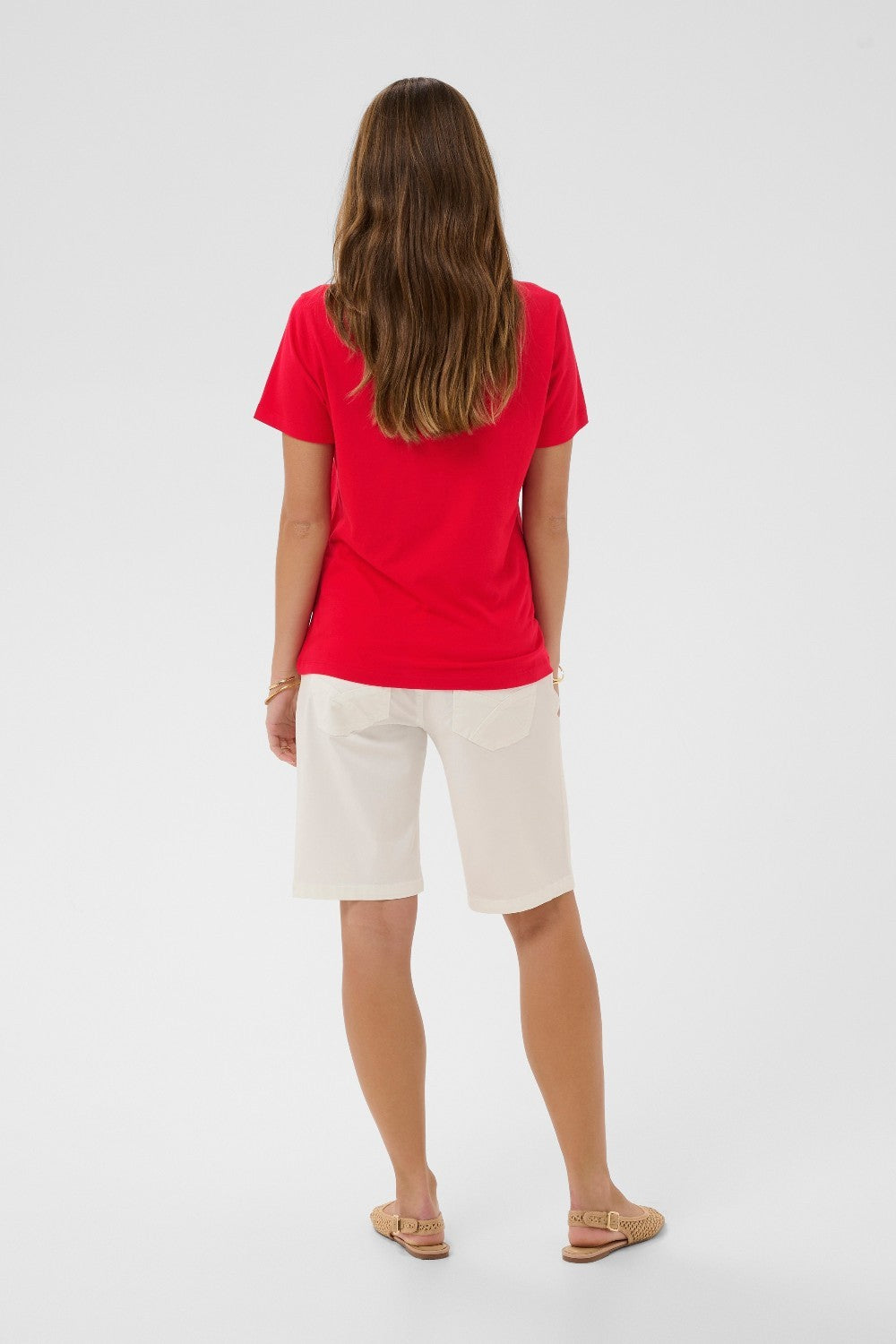 Woman wearing a red shirt and white shorts on a plain background