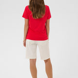 Woman wearing a red shirt and white shorts on a plain background
