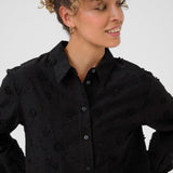 Woman wearing a black embroidered shirt against a white background