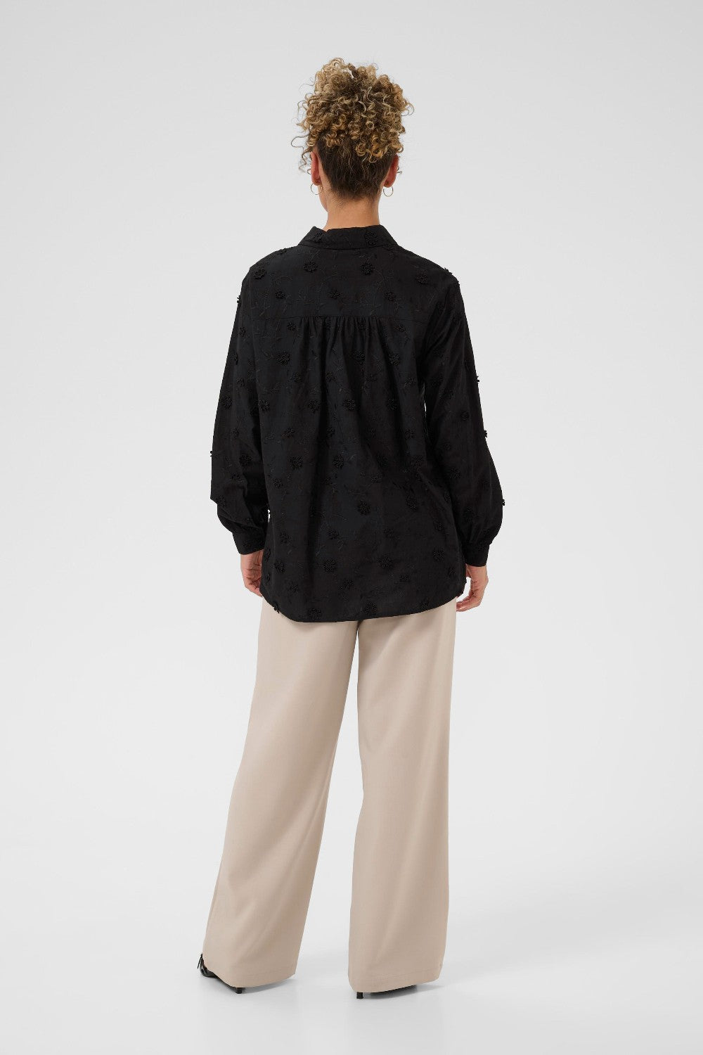 Person wearing a black shirt and beige pants on a white background