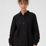 Woman wearing a black button-up shirt with a subtle pattern on a white background