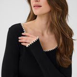 Woman wearing a black sweater with white trim on a plain background