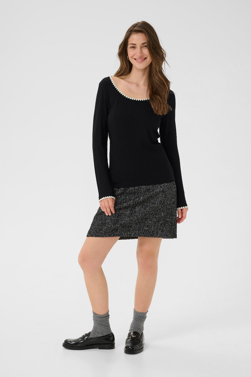 Woman wearing a black sweater and gray skirt on a white background