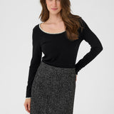 Woman wearing a black long-sleeve top and patterned skirt on a white background