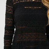 Black patterned top worn by a person on a white background