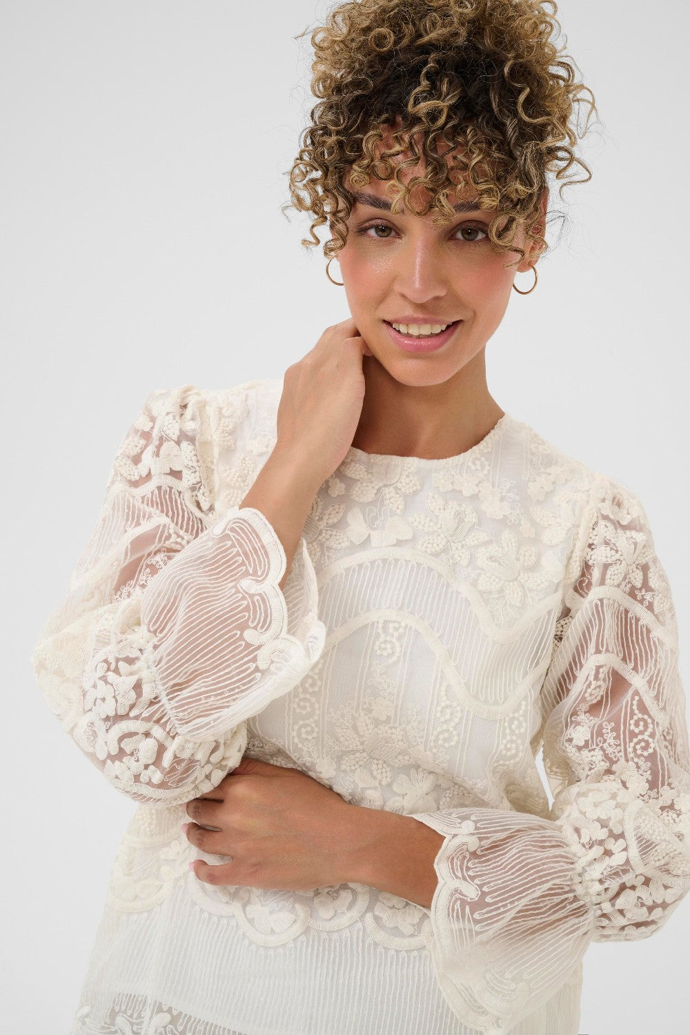 Woman wearing a white lace top against a plain background